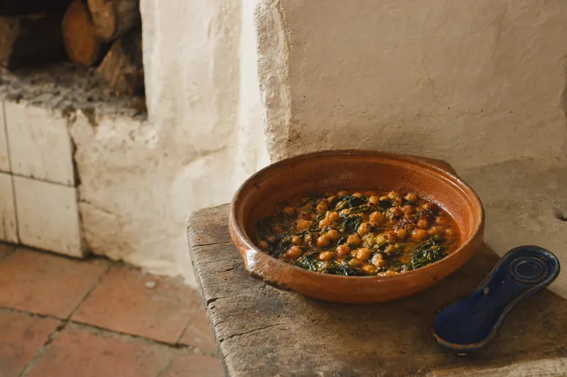 Spanische Tonkasserolle mit lange geschmorten Kichererbsen, Spinat und geräuchertem Paprika auf einem abgenutzten Holzbrett