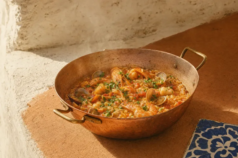 Portugiesischer Arroz de marisco in einer flachen Kupferpfanne: glänzender Tomatenreis mit Muscheln