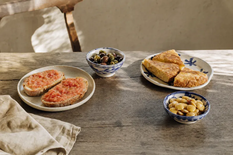 Kleine Auswahl iberischer Tapas und Petiscos auf verwittertem Holz, darunter Pan con tomate